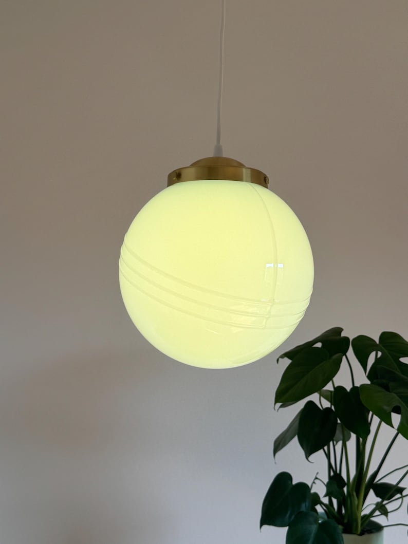 May include: A white globe pendant light with a brass fixture. The globe has a textured surface with lines running across it.