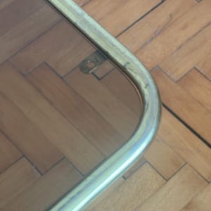 May include: Close-up of the corner of a glass table top with a brass frame. The frame has a rounded edge and a small metal bracket.
