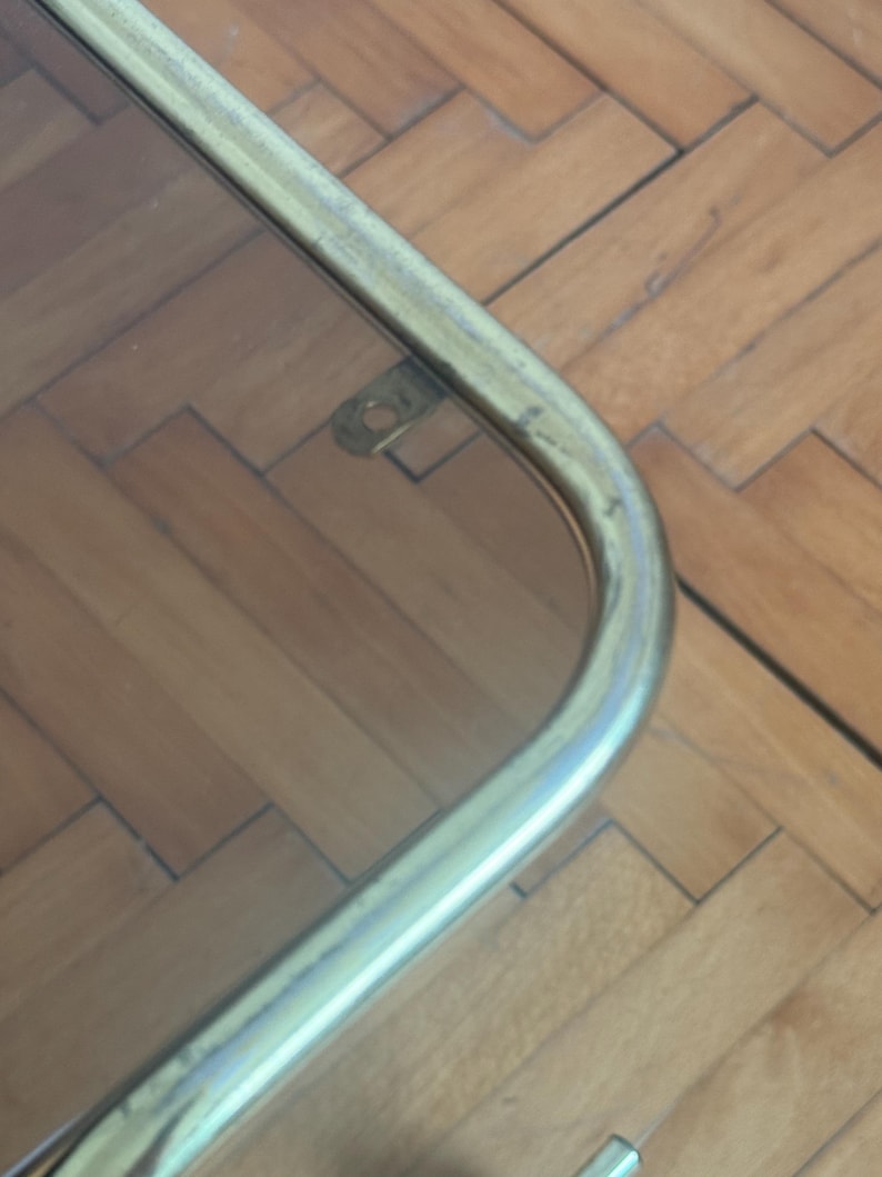 May include: Close-up of the corner of a glass table top with a brass frame. The frame has a rounded edge and a small metal bracket.