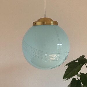 May include: A light blue glass globe pendant light with a brass fixture. The globe has a subtle ribbed texture.