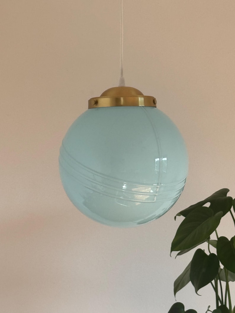 May include: A light blue glass globe pendant light with a brass fixture. The globe has a subtle ribbed texture.