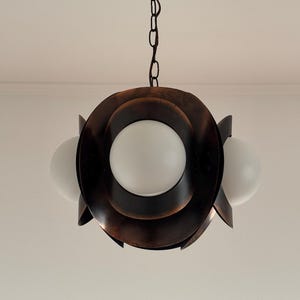 Puede incluir: Una l&aacute;mpara colgante de tono cobre con tres globos de vidrio blanco. La l&aacute;mpara tiene un dise&ntilde;o circular con capas superpuestas.