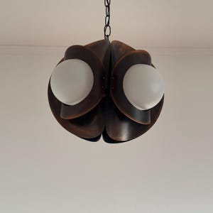 Puede incluir: Una l&aacute;mpara colgante de metal marr&oacute;n con una cadena que cuelga del techo. La l&aacute;mpara tiene un dise&ntilde;o &uacute;nico con m&uacute;ltiples capas superpuestas, creando una forma de flor. Se pueden ver dos bombillas blancas en forma de globo.