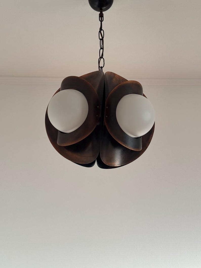 Puede incluir: Una l&aacute;mpara colgante de metal marr&oacute;n con una cadena que cuelga del techo. La l&aacute;mpara tiene un dise&ntilde;o &uacute;nico con m&uacute;ltiples capas superpuestas, creando una forma de flor. Se pueden ver dos bombillas blancas en forma de globo.