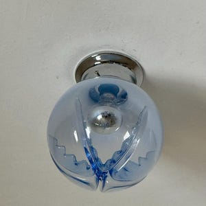 May include: A light blue, globe-shaped ceiling light fitting with a chrome base. The glass globe has a decorative, scalloped design and houses a visible lightbulb. The fitting is mounted on a white ceiling.