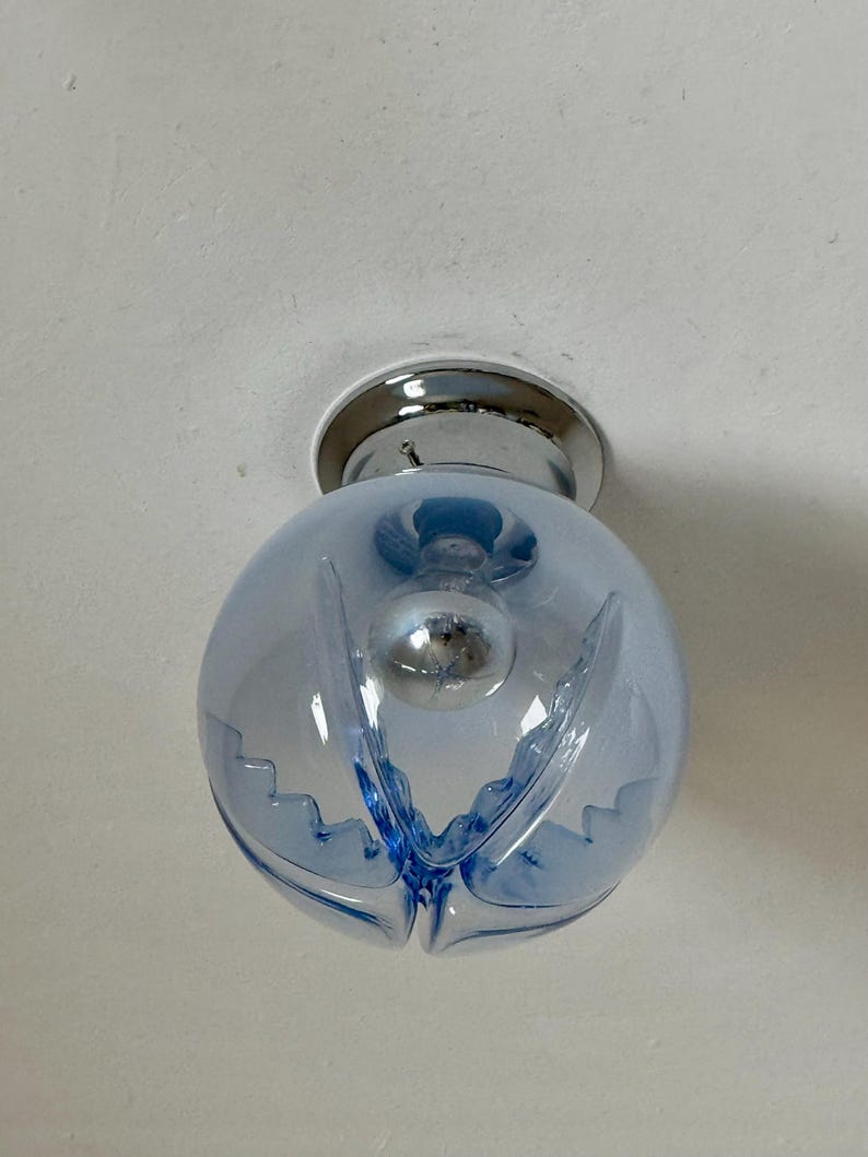May include: A light blue, globe-shaped ceiling light fitting with a chrome base. The glass globe has a decorative, scalloped design and houses a visible lightbulb. The fitting is mounted on a white ceiling.