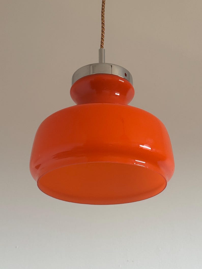 May include: Orange glass pendant light with a chrome finish. The light has a rounded, bulbous shape.