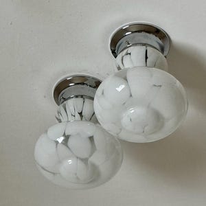 May include: Two flush mount ceiling lights with chrome bases and white glass globes. The globes have a marbled pattern of white and translucent glass. The lights are mounted on a white ceiling.