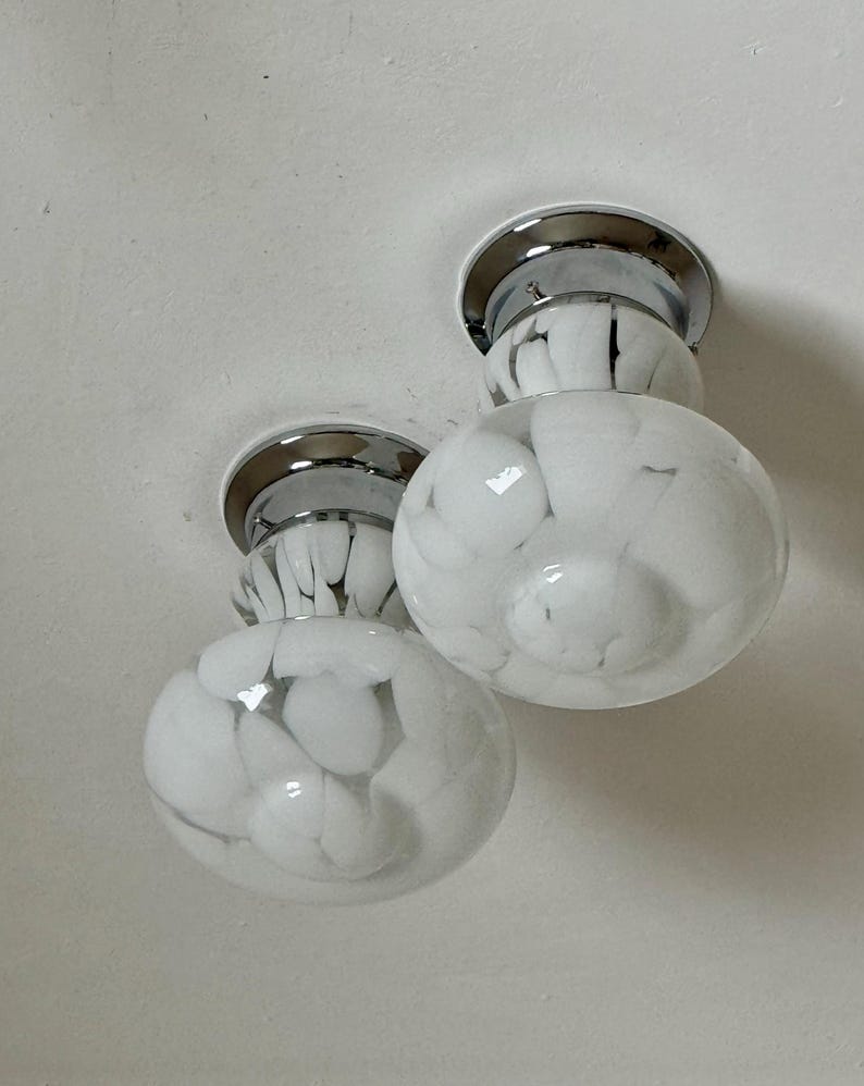 May include: Two flush mount ceiling lights with chrome bases and white glass globes. The globes have a marbled pattern of white and translucent glass. The lights are mounted on a white ceiling.