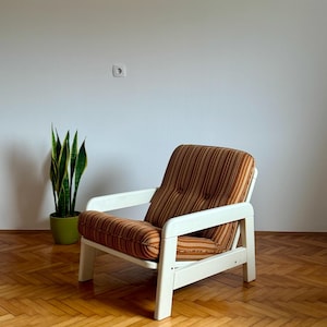May include: A white and brown striped armchair with a white wooden frame. The chair is sitting on a wooden floor.