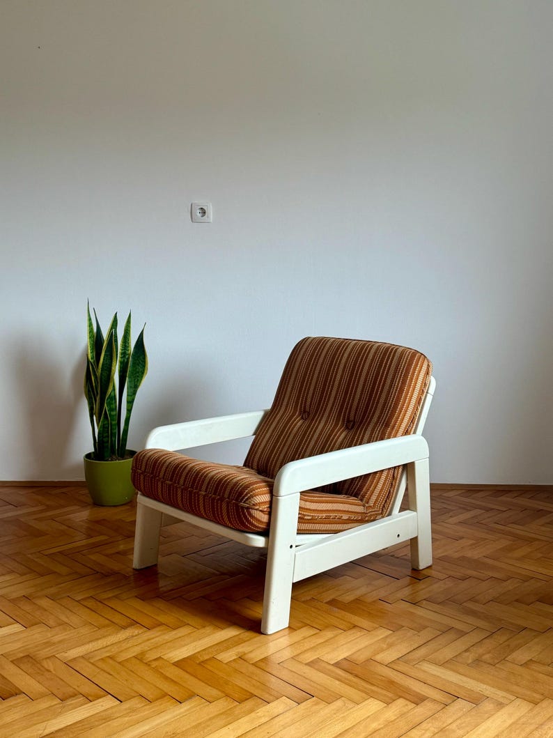 May include: A white and brown striped armchair with a white wooden frame. The chair is sitting on a wooden floor.