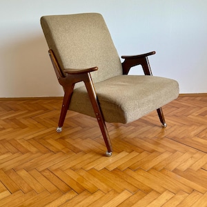 May include: A mid-century modern armchair with a brown fabric upholstery and wooden frame. The chair has a unique design with angled legs and arms. The chair is sitting on a wooden floor.