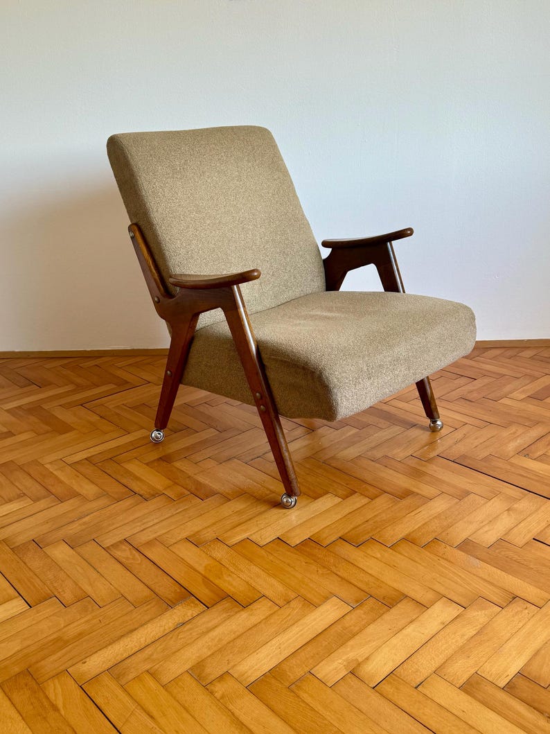 May include: A mid-century modern armchair with a brown fabric upholstery and wooden frame. The chair has a unique design with angled legs and arms. The chair is sitting on a wooden floor.