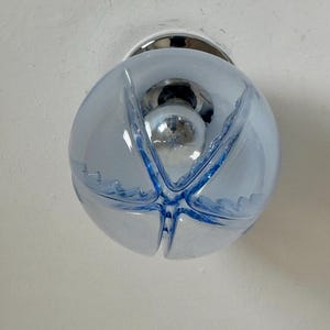 May include: A light blue glass globe light fitting with a chrome base. The globe has a starburst design in darker blue and a chrome bulb inside. The fitting is mounted on a white ceiling.
