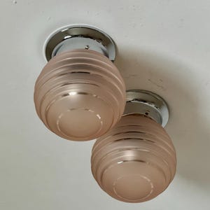 May include: Two ceiling-mounted light fixtures. Each fixture has a chrome base and a frosted, peach-colored glass shade with horizontal ridges. The shades are spherical in shape.