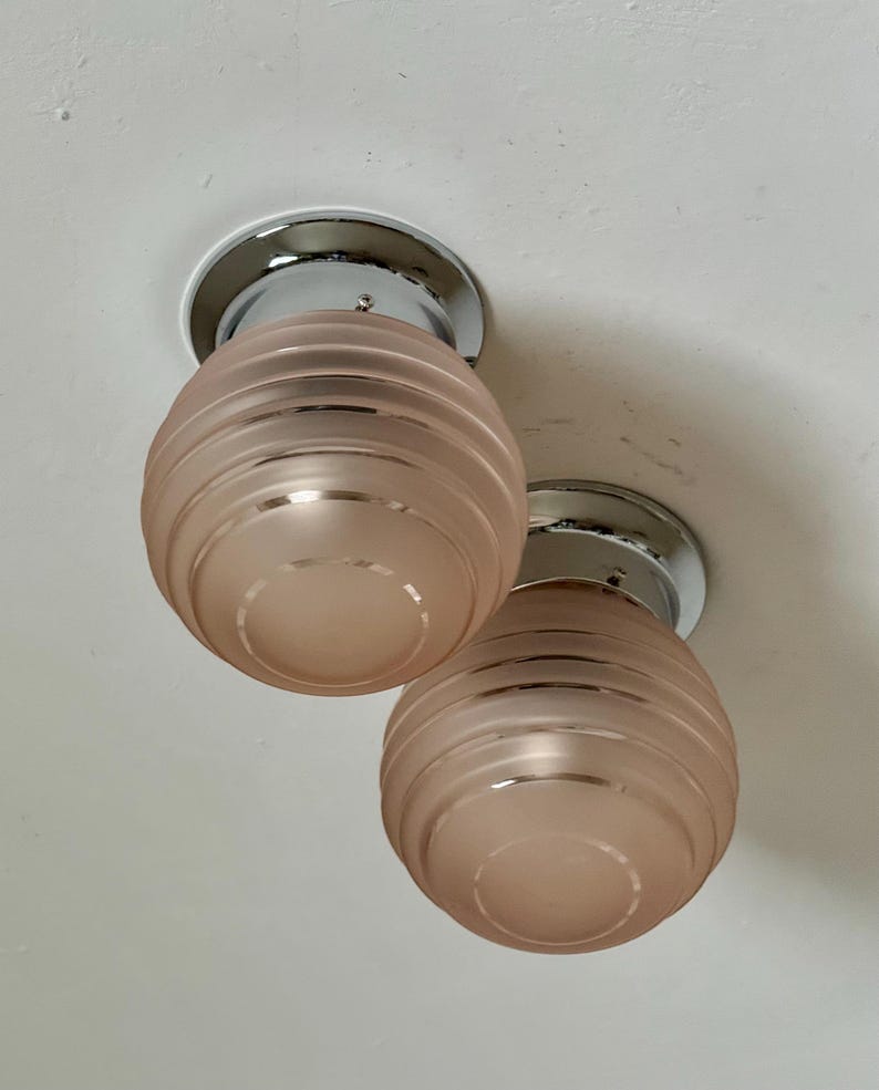 May include: Two ceiling-mounted light fixtures. Each fixture has a chrome base and a frosted, peach-colored glass shade with horizontal ridges. The shades are spherical in shape.