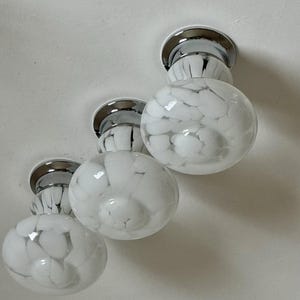 May include: Three flush-mount ceiling lights with chrome bases and white, marbled glass globes. The globes have a round shape and a pattern of white swirls. The lights are mounted on a white ceiling.