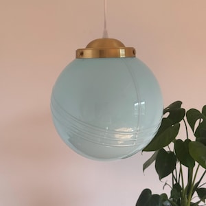 May include: A light blue glass globe pendant light with a gold metal top. The light is hanging from a white cord.