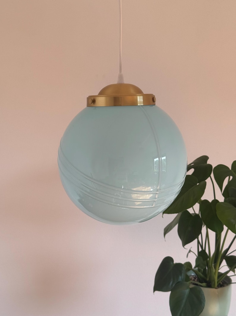 May include: A light blue glass globe pendant light with a gold metal top. The light is hanging from a white cord.