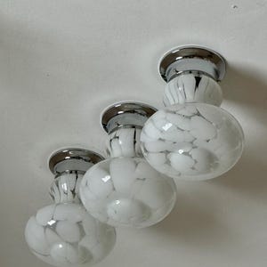 May include: Three white and chrome ceiling lights with a speckled pattern. Each light has a round, globe-shaped shade with a chrome base and a circular chrome accent. The lights are mounted on a white ceiling.