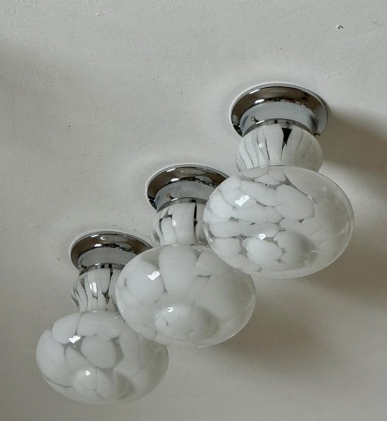 May include: Three white and chrome ceiling lights with a speckled pattern. Each light has a round, globe-shaped shade with a chrome base and a circular chrome accent. The lights are mounted on a white ceiling.