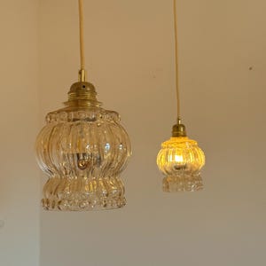 May include: Two clear glass pendant lights with gold metal fixtures hanging from white ceilings. The lights are turned on and emitting a warm yellow glow.