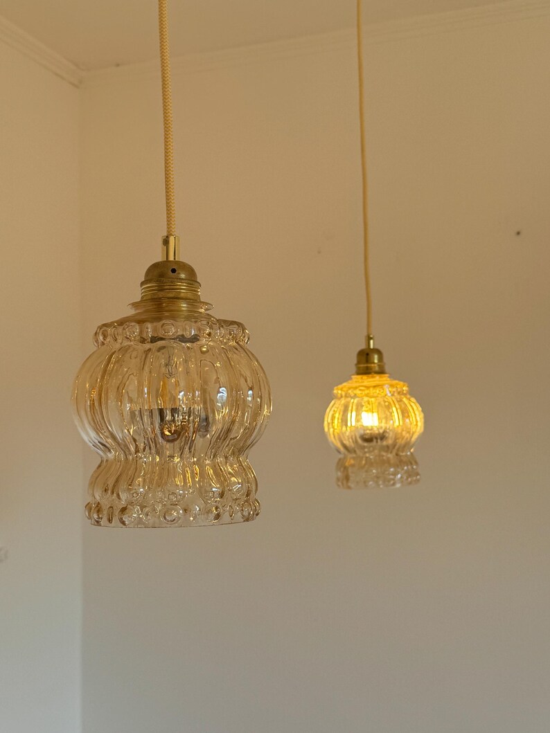 May include: Two clear glass pendant lights with gold metal fixtures hanging from white ceilings. The lights are turned on and emitting a warm yellow glow.