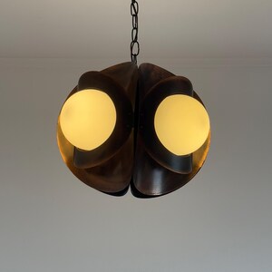 Puede incluir: Una l&aacute;mpara colgante de estilo moderno de mediados de siglo con forma esf&eacute;rica. La l&aacute;mpara est&aacute; hecha de madera marr&oacute;n oscura y presenta dos globos de vidrio blanco esmerilado.