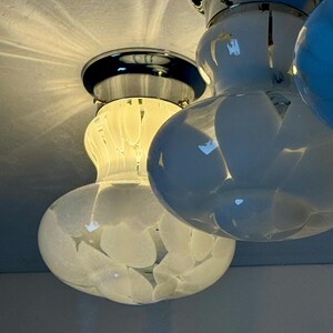 May include: Close-up of a ceiling light fixture with three glass globes. The globes are white with a speckled pattern and are attached to a chrome base. The light is on, illuminating the room.