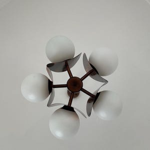 May include: A five-light chandelier with a modern design. The chandelier has a dark brown metal frame with five white globe-shaped light bulbs.