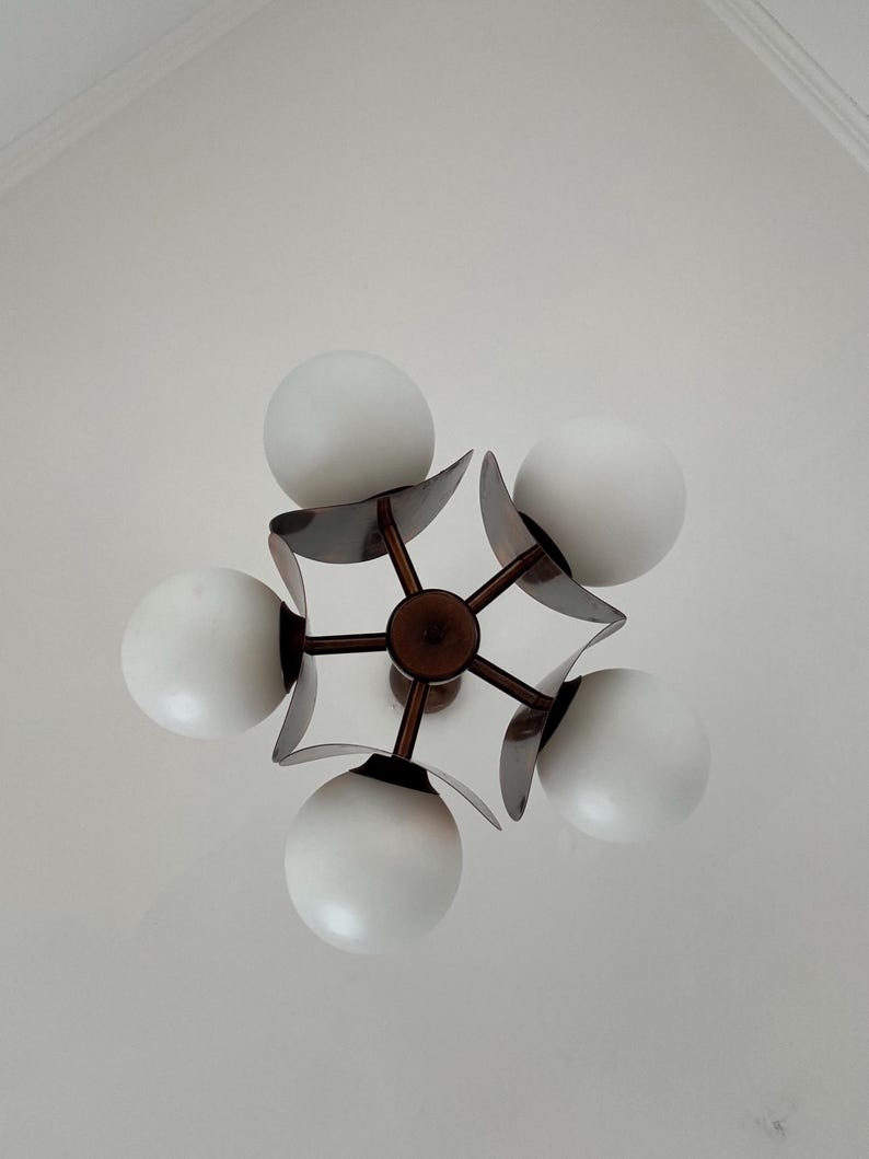 May include: A five-light chandelier with a modern design. The chandelier has a dark brown metal frame with five white globe-shaped light bulbs.