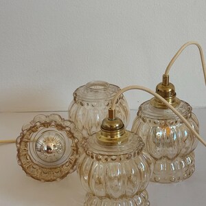 May include: Three amber glass pendant lights with a textured, ribbed design and gold metal accents. The lights are hanging from white cords.