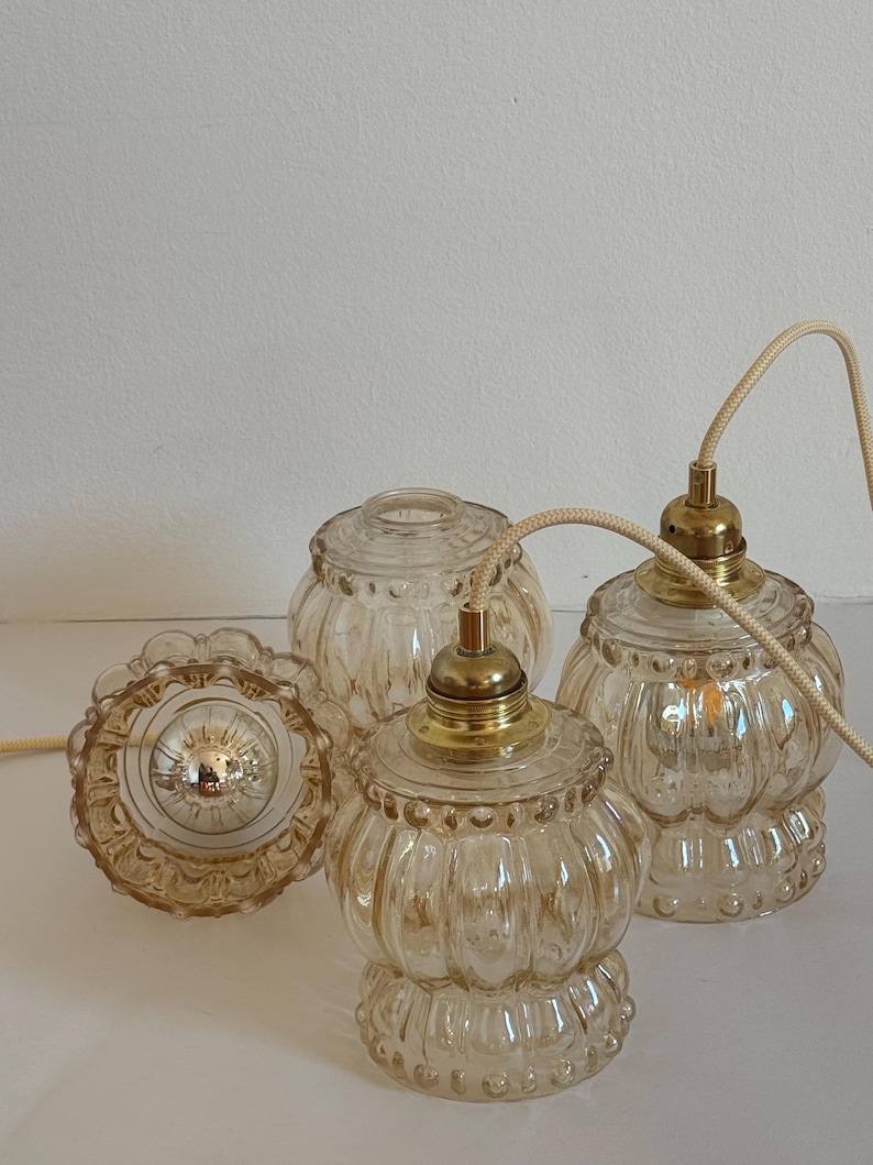May include: Three amber glass pendant lights with a textured, ribbed design and gold metal accents. The lights are hanging from white cords.