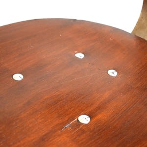 Puede incluir: Primer plano de un asiento de silla de madera con cuatro tornillos plateados visibles. El asiento est&aacute; hecho de madera oscura con un acabado liso.