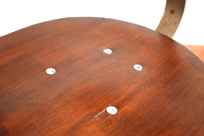 Puede incluir: Primer plano de un asiento de silla de madera con cuatro tornillos plateados visibles. El asiento est&aacute; hecho de madera oscura con un acabado liso.