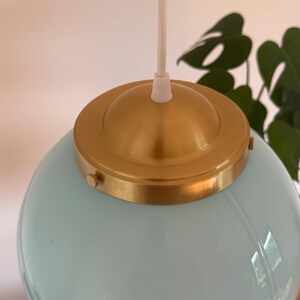 May include: A light blue glass globe pendant light with a brass ceiling fixture and a white cord.