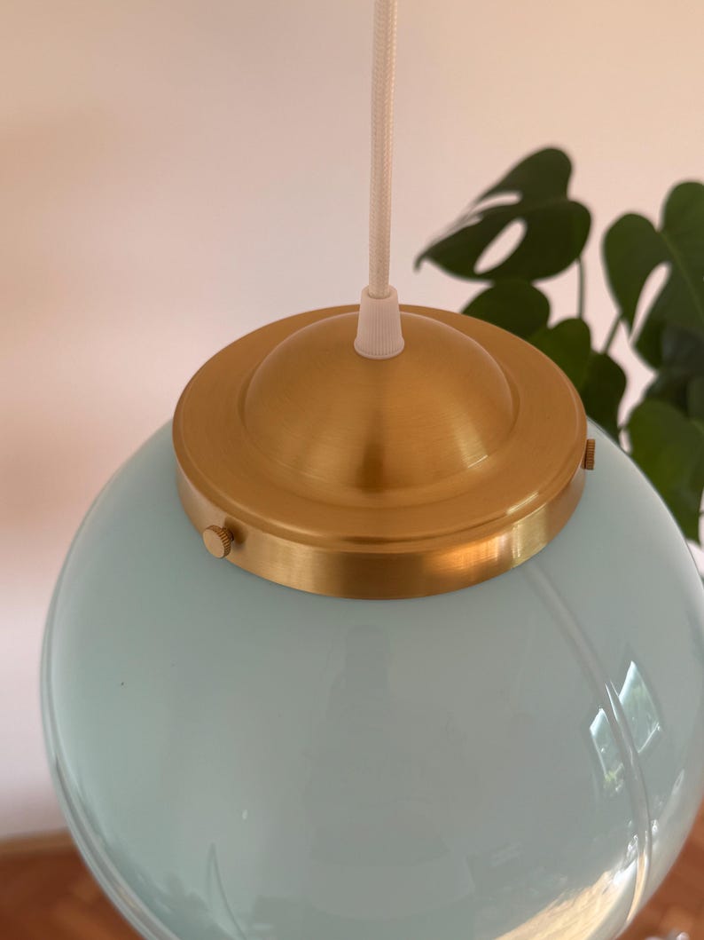 May include: A light blue glass globe pendant light with a brass ceiling fixture and a white cord.