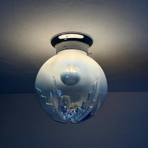 May include: A spherical, blue glass ceiling light with a chrome base. The glass shade features a distinctive, cut-out pattern and contains a visible light bulb. The fixture is mounted on a white ceiling.