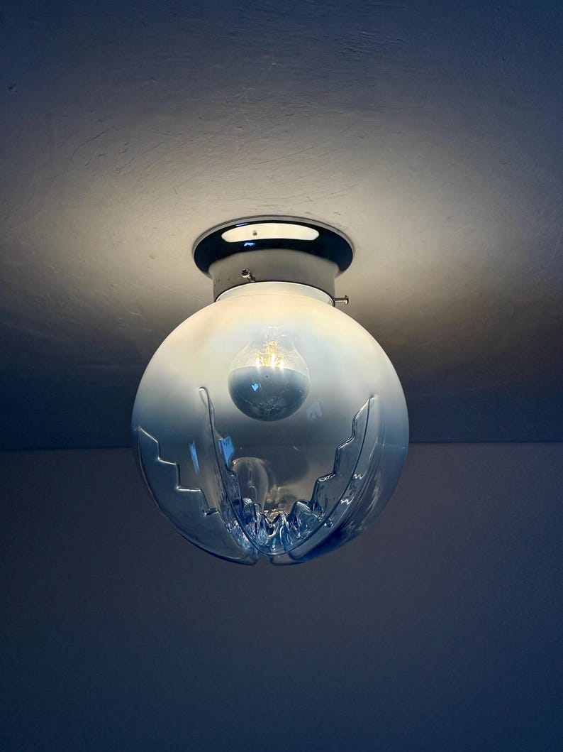 May include: A spherical, blue glass ceiling light with a chrome base. The glass shade features a distinctive, cut-out pattern and contains a visible light bulb. The fixture is mounted on a white ceiling.