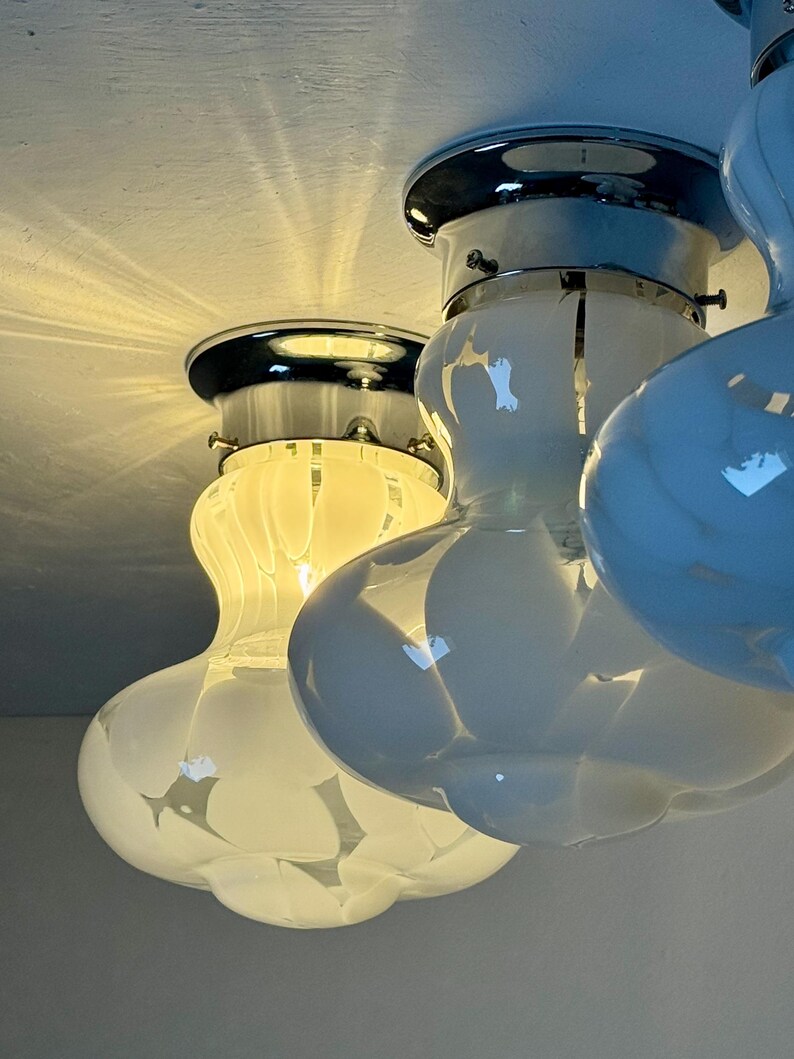 May include: Close-up of three white and chrome ceiling lights. Each light has a bulbous, rounded shape with a chrome base and a white glass shade. The lights are mounted on a white ceiling, with light reflecting off the surfaces.