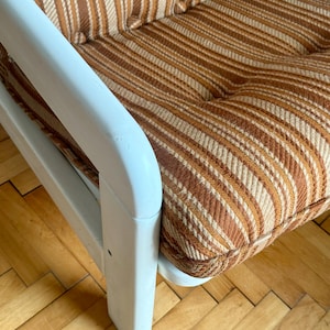 May include: A white wooden armchair with brown and white striped upholstery. The chair has a simple design with a high back and wide arms.