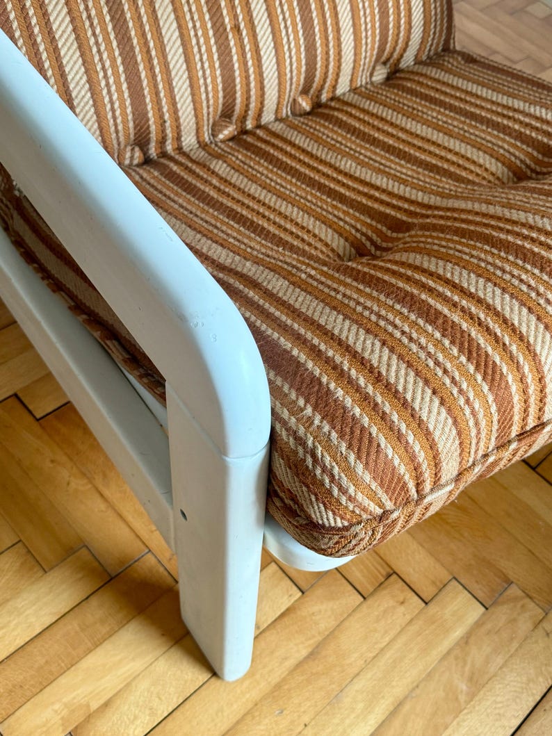 May include: A white wooden armchair with brown and white striped upholstery. The chair has a simple design with a high back and wide arms.