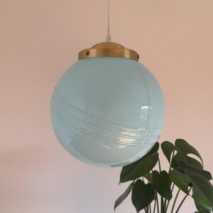 May include: A light blue glass globe pendant light with a brass fixture. The globe has a textured surface.