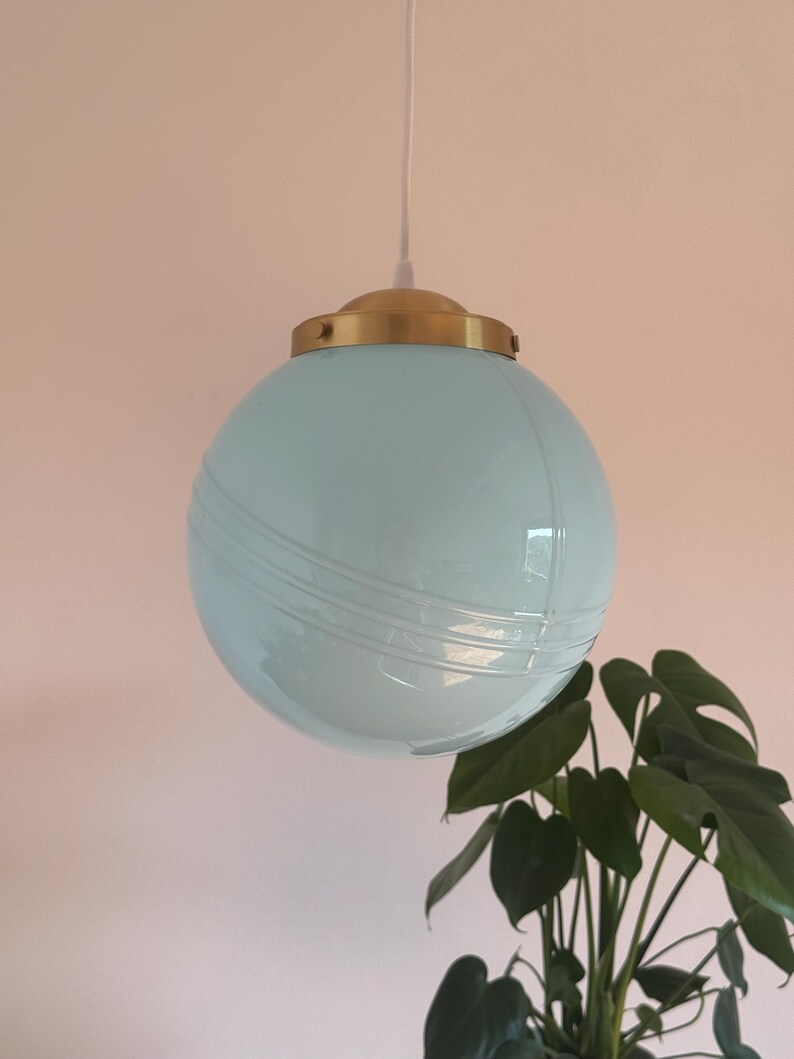 May include: A light blue glass globe pendant light with a brass fixture. The globe has a textured surface.