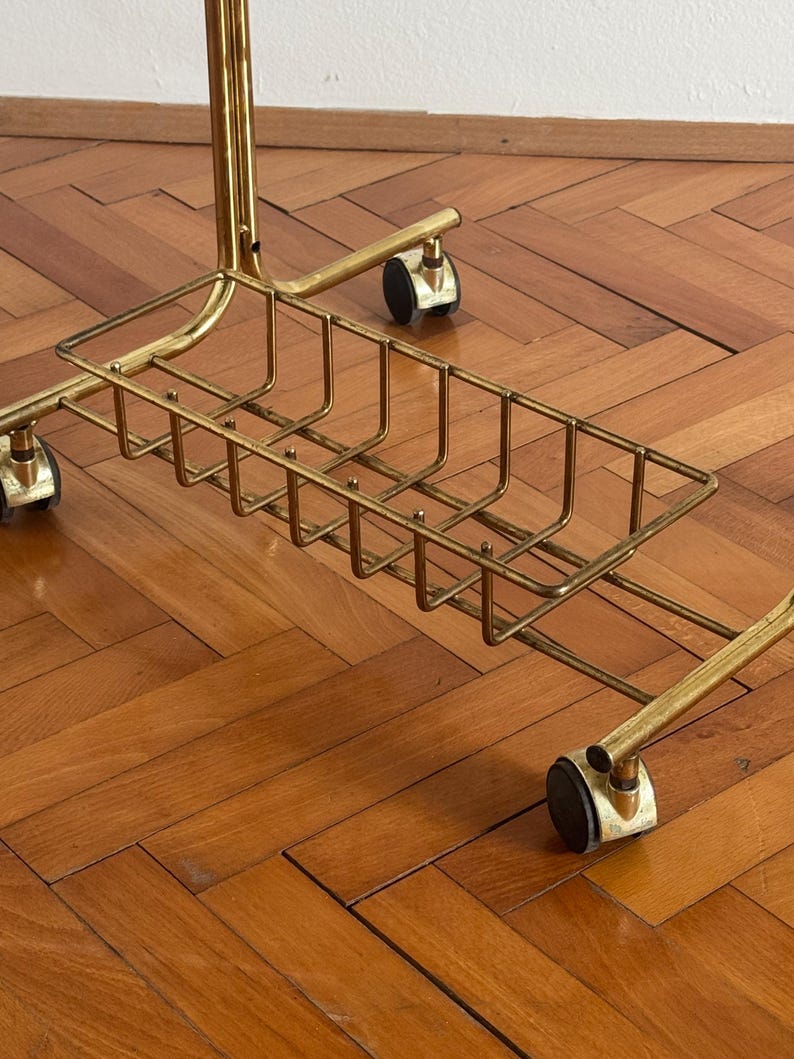 May include: A gold metal rolling stand with a wire basket underneath. The stand has four wheels and is on a wooden floor.