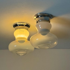 Könnte beinhalten: Zwei weiße Glas-Deckenleuchten mit verchromten Akzenten. Die Leuchten sind eingeschaltet und beleuchten den Raum.