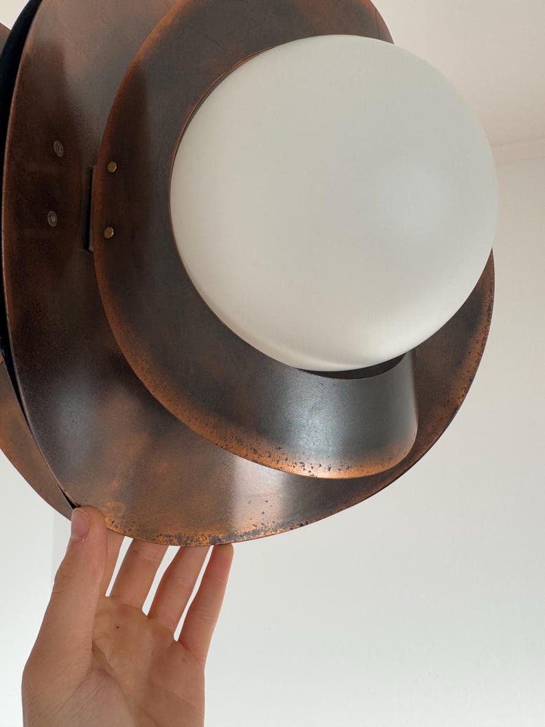 Puede incluir: Una l&aacute;mpara colgante de tono cobre con una pantalla de vidrio blanco. La l&aacute;mpara tiene un dise&ntilde;o en capas y org&aacute;nico.