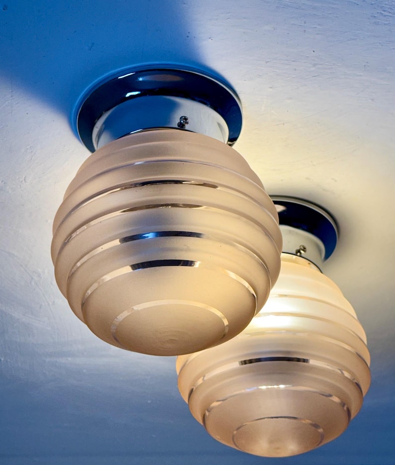 May include: Two Art Deco-style ceiling light fixtures. Each fixture has a frosted glass globe with horizontal bands, a chrome base, and a dark blue circular mounting plate. The lights are mounted on a white ceiling.
