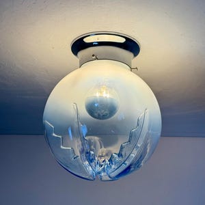 May include: A blue and clear glass globe light fitting with a chrome base. The globe has a decorative cut design and contains a light bulb. The fitting is mounted on a white ceiling.