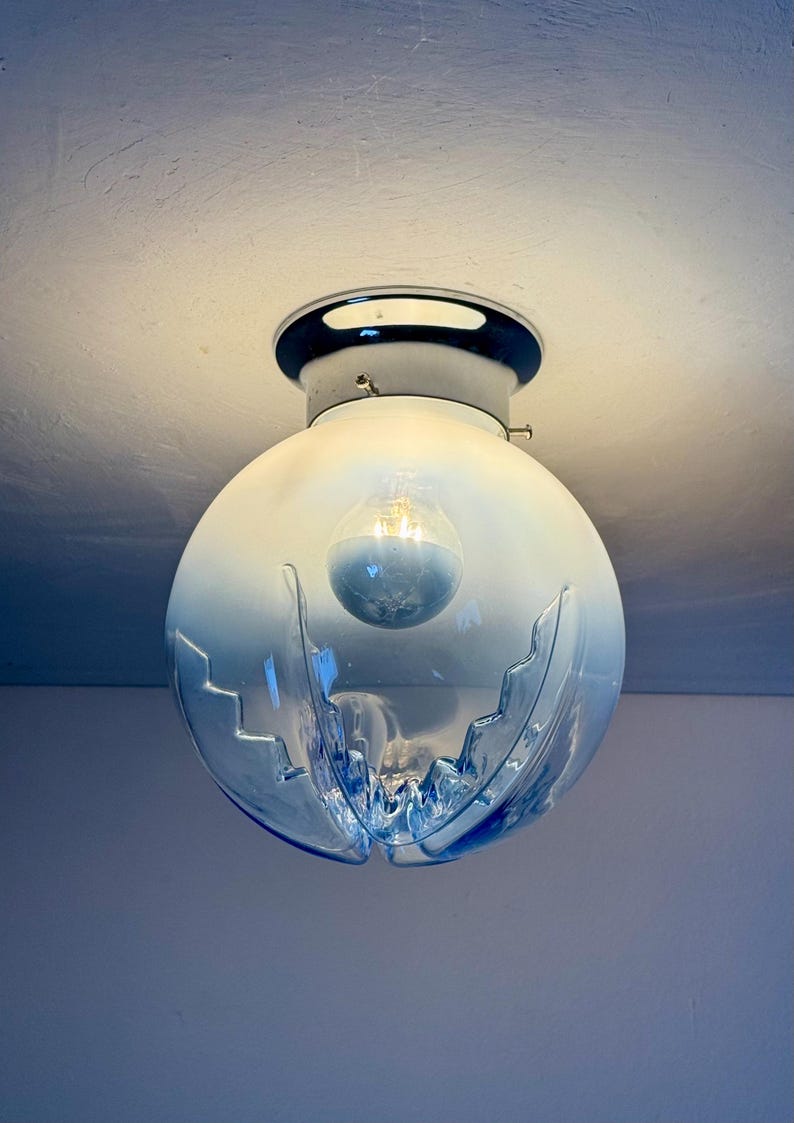 May include: A blue and clear glass globe light fitting with a chrome base. The globe has a decorative cut design and contains a light bulb. The fitting is mounted on a white ceiling.